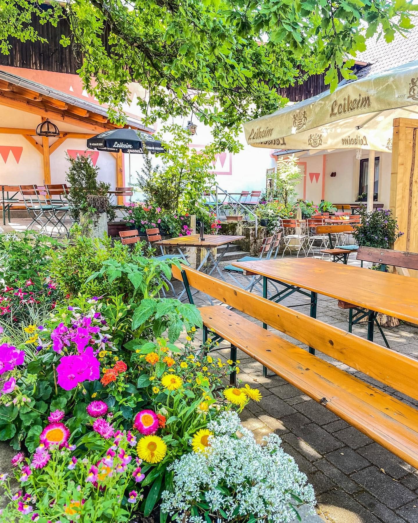 Blühende Beete vor Biertischen unter Sonnenschirmen