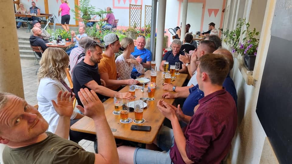Lange Tafel mit Gästen und Bierkrügen unter dem Vordach